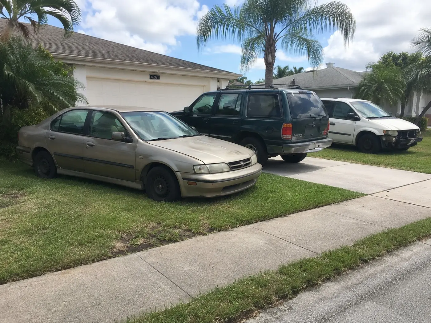 A junk sedan on the grass beside an old SUV and a damaged minivan