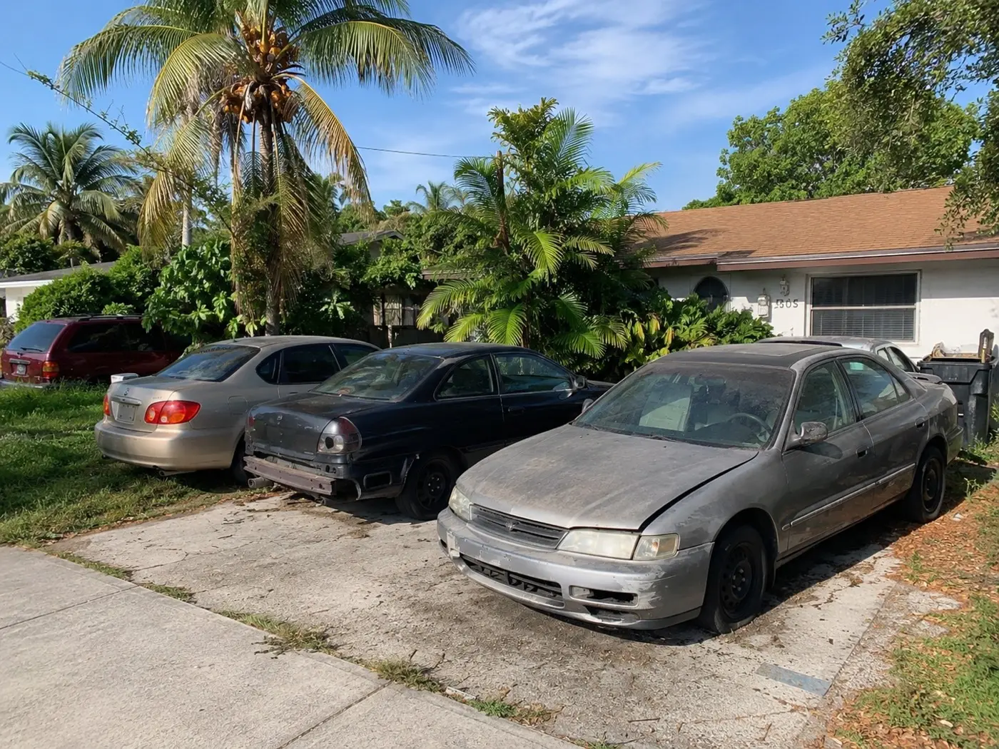 Dust-covered junk cars in a driveway, one missing its rear bumper
