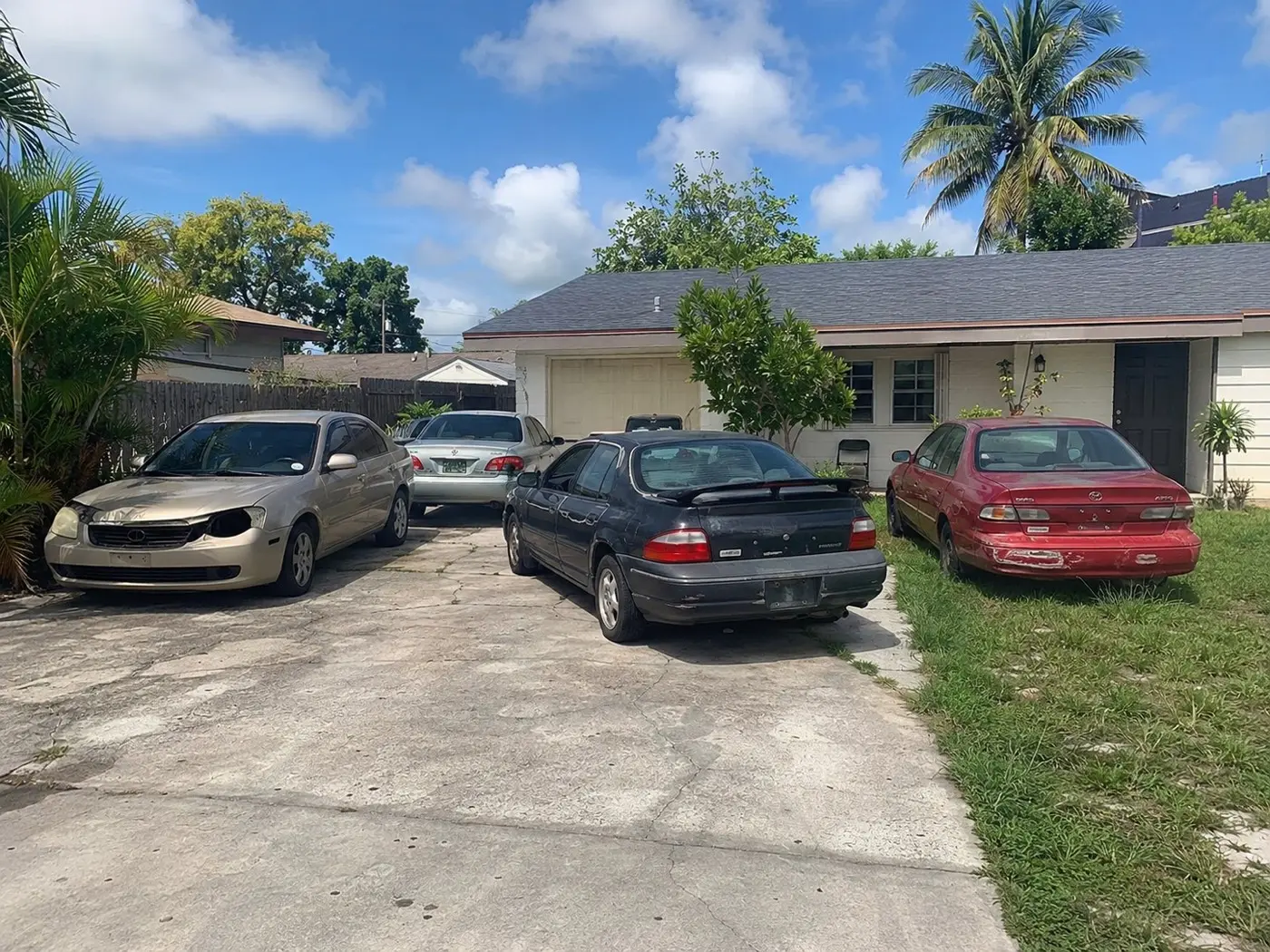 Three junk cars parked on a cracked concrete driveway outside a Florida home