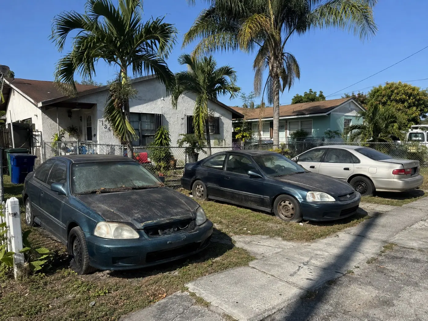 Two derelict Hondas sitting on a front lawn behind a chain-link fence