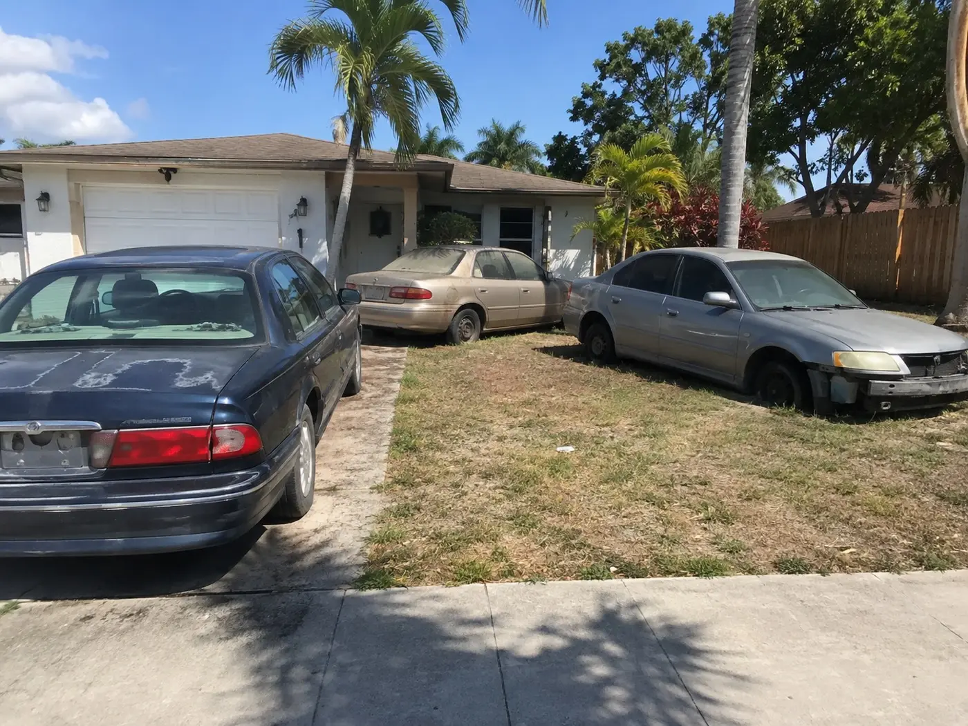 Junk sedans parked across the grass and driveway of a Florida house