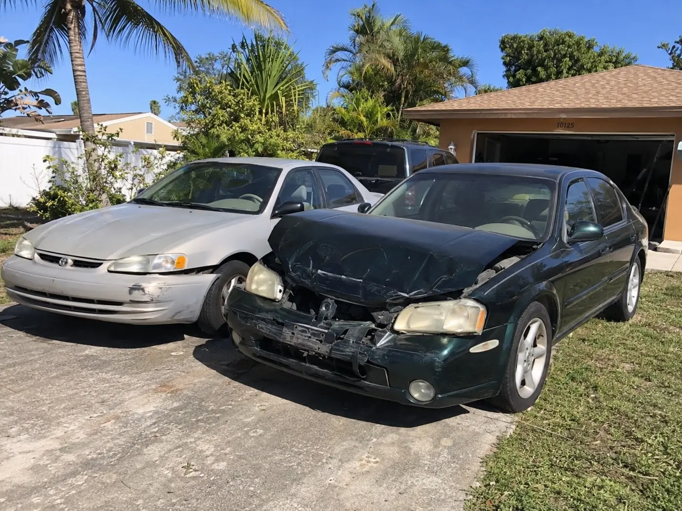 A sedan with heavy front-end collision damage parked next to another car